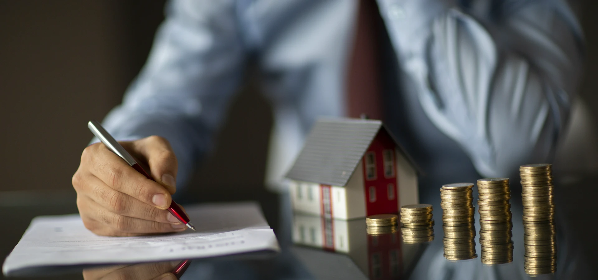 mężczyzna podpisujący dokument przy makiecie domku